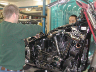 Two men standing next to a motorcycle part
